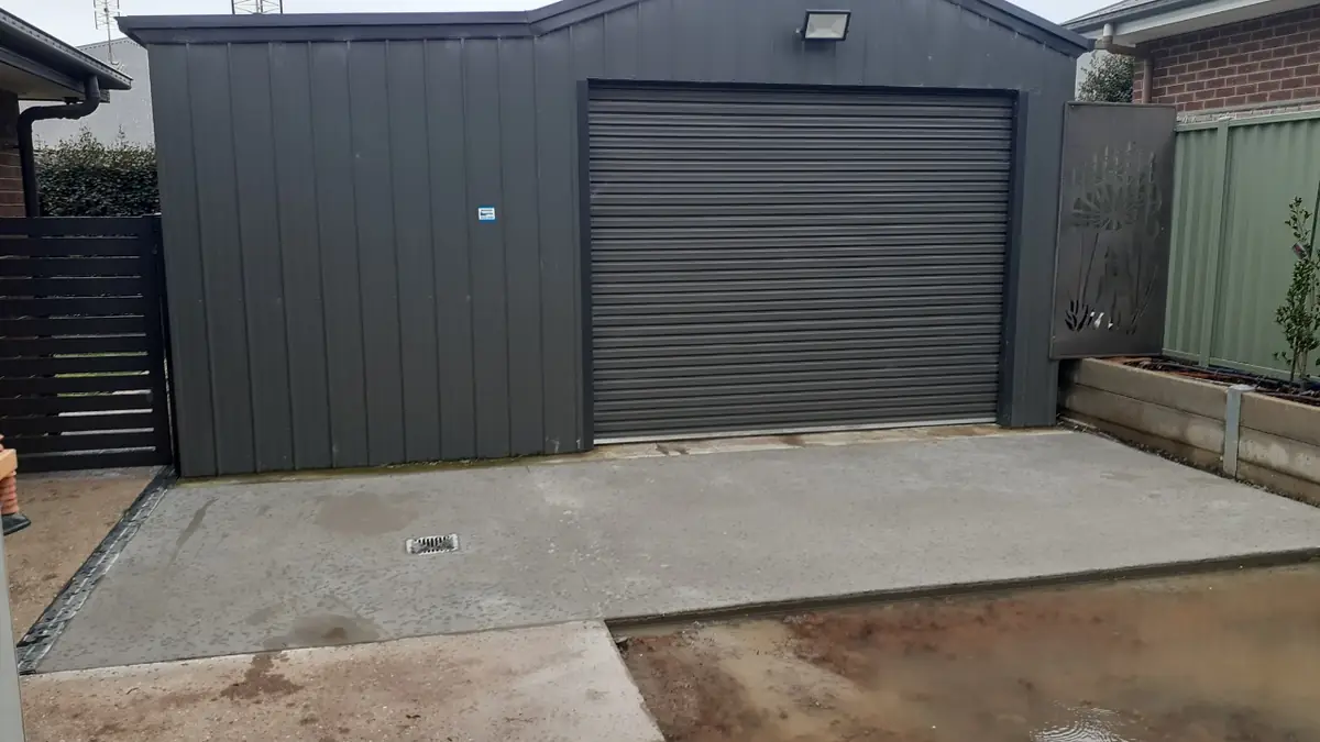 Finished concrete driveway in front of a dark steel shed with a roller door
